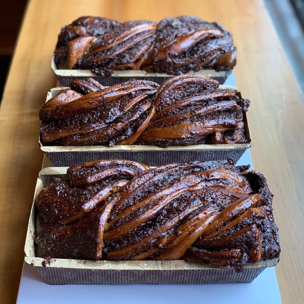 Three freshly baked chocolate babka loaves in paper baking molds on a wooden surface.