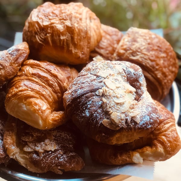 A close-up of golden-brown croissants, some dusted with powdered sugar and sliced almonds, on a tray.